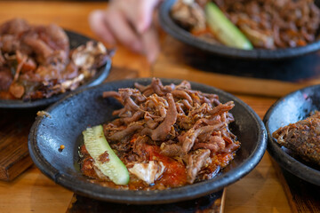 Crispy fried chicken intestines (Usus Goreng) with spicy Indonesian sambal and fresh cucumber slice, served in a traditional stone mortar (cobek). A popular, savory street food.