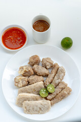 A plate of Siomay, a popular Indonesian street food, featuring steamed fish dumplings, tofu, and fish cakes with sliced lime. A bowl of chili sauce and a mug of peanut sauce are also visible.