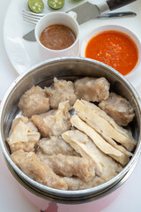 Various steamed Indonesian siomay and tofu pieces are shown in a metal pot, with cups of peanut sauce and chili sauce in the blurred background.