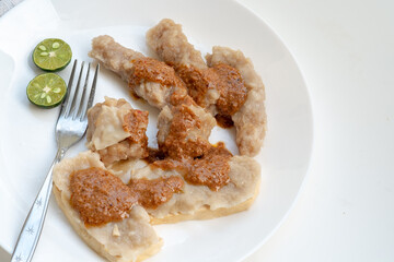 A serving of traditional Indonesian siomay, featuring fish dumplings and steamed tofu filled with fish cake, all topped with peanut sauce on a white plate.