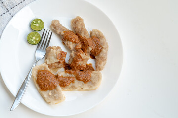 A serving of traditional Indonesian siomay, featuring fish dumplings and steamed tofu filled with fish cake, all topped with peanut sauce on a white plate.