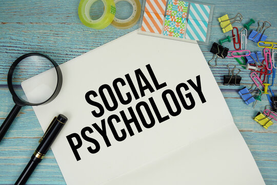 Social Psychology text on a paper surrounded by office supplies and magnifying glass on a blue wooden surface