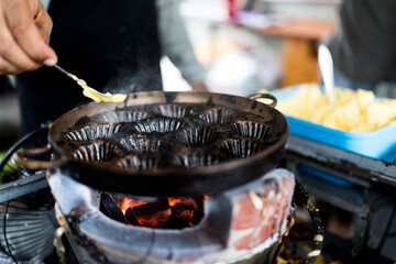 A Thai trader spread butter in hot pan to make oval sweetmeat