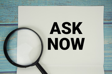 Ask Now text written on notepad with magnifying glass flat lay on wooden background