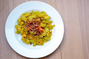 A dish of stir-fried bitter melon (tumis pare) and egg with small dried anchovies and red chili on...