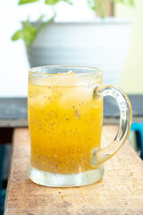 A sweating glass mug of iced orange juice with hydrating basil seeds (biji selasih) sits on a rustic wooden plank, featuring a bright, tropical, and refreshing summer look.