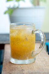A sweating glass mug of iced orange juice with hydrating basil seeds (biji selasih) sits on a rustic wooden plank, featuring a bright, tropical, and refreshing summer look.