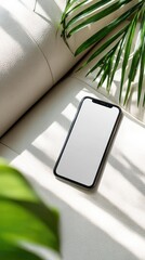 Blank screen smartphone on luxury white leather couch with a green indoor plant. Flatlay top view mockup