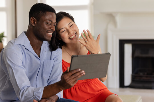 Happy couple video chatting, showing engagement ring, sitting together at home - Powered by Adobe