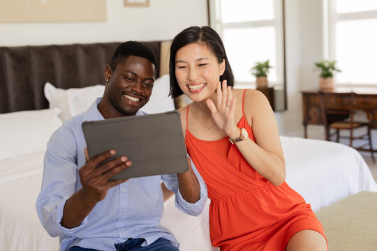 Smiling couple using tablet for video call in cozy bedroom setting