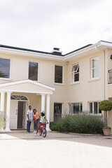 Family enjoying time outside home while child rides bicycle in driveway