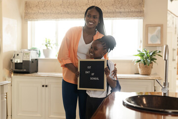 Holding first day of school sign, African American mother and daughter smiling at home