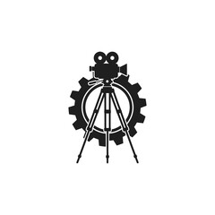 A black silhouette icon of a vintage film camera on a tripod in front of a large mechanical gear.