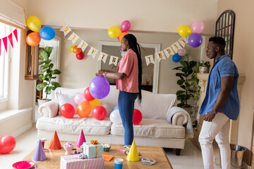 Decorating living room with balloons, African American couple preparing birthday celebration