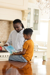 Obraz premium African American father reading storybook to son in cozy kitchen setting