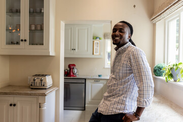African American man smiling while leaning against kitchen counter at home