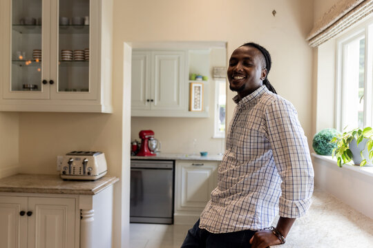 African American man smiling while leaning against kitchen counter at home