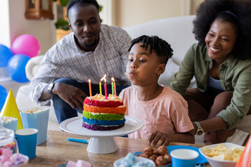 Blowing out candles on colorful cake, African American boy with smiling parents