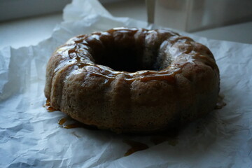Homemade bundt cake with glaze on parchment paper, rustic autumn dessert near window, cozy seasonal baking symbolizing warmth, comfort, and homemade tradition.