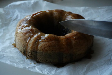 Close-up of a homemade bundt cake being sliced with a knife, fresh baked dessert with golden crust, traditional sweet pastry for breakfast or holiday celebration.