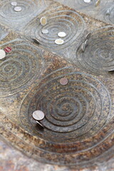 Coins placed on spiral engravings in a temple for good luck and blessings, traditional Buddhist ritual in Thailand symbolizing fortune, faith, and prosperity.