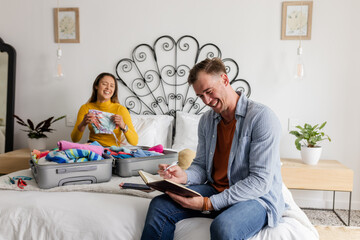Couple packing suitcase on bed, smiling and planning vacation together
