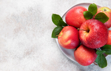 Fresh red apples with green leaves on white plate
