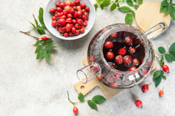 Steaming rosehip tea brewing in glass teapot with fresh rose hips