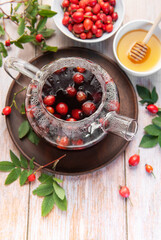 Steaming rosehip tea brewing in glass teapot with honey and fresh rose hips