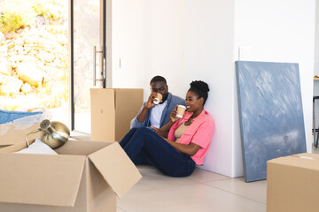 Couple enjoying coffee break while unpacking boxes in new home, feeling relaxed