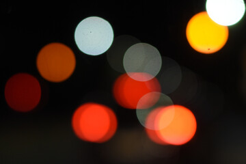 City night bokeh with glowing traffic lights, artistic defocused background. Abstract car lights, glowing bokeh circles on dark background.