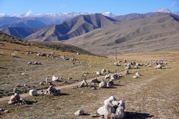 A wide view of a mountainous landscape featuring scattered rocks and stones on dry grass....