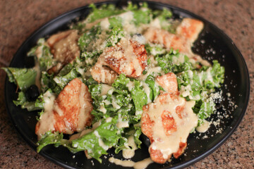 Gourmet Caesar salad with grilled chicken, romaine, parmesan on black plate.