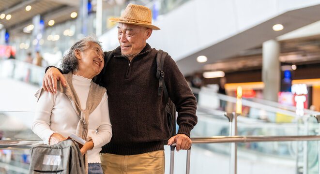 Senior asian traveler couple smiling at airport with suitcases show excitement before travel, retirement lifestyle, planning international journey, travel insurance for elderly, tour and global trip