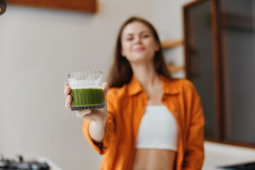 Young woman in an orange jacket holds a green smoothie, promoting healthy eating and wellness in a...