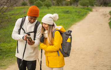 Multiethnic couple of hikers using smartphone gps app for navigating on hiking trail, travel and adventure concept with copy space
