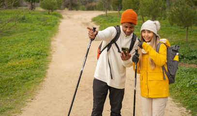 Multiethnic couple of hikers using smartphone and checking map during trekking day in nature with copy space