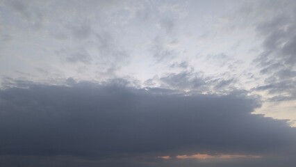 A serene sky scene at dawn, with a thick band of dark, heavy clouds covering the lower half and a lighter, scattered cloud layer above. A hint of light breaks through below.