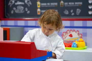 Little chef playing with cash register in toy kitchen
