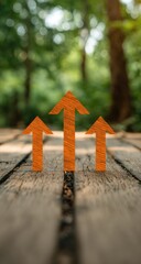 Three orange arrows pointing upward on a wooden surface, with a blurred green forest background