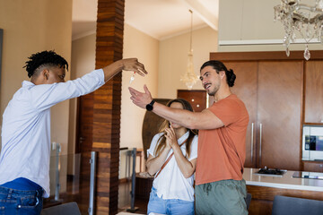 Friends celebrating new home, exchanging keys with excitement in modern kitchen