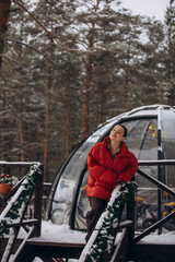 Naklejka premium A beautiful woman is relaxing in the forest in winter glamping on the background of a domed tent
