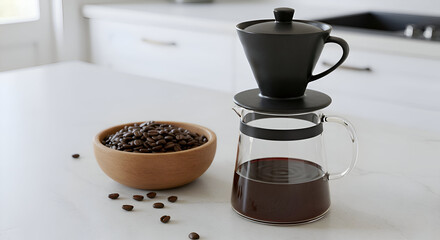 A modern coffee maker with a glass carafe and black pour-over filter sits on a light gray countertop. Coffee beans are in a wooden bowl next to the brewing apparatus.