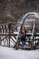 A beautiful woman is relaxing in the forest in winter glamping on the background of a domed tent