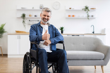Senior Caucasian man seated in wheelchair showing thumbs-up gesture expressing positivity indoors....