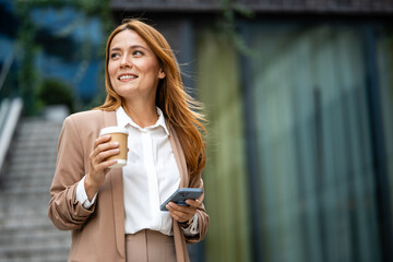 Businesswoman holding coffee and smartphone, walking in the city