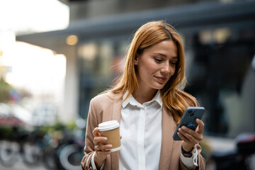 Businesswoman using smartphone and holding coffee outside office building