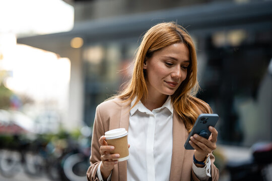 Businesswoman using smartphone and holding coffee outside office building