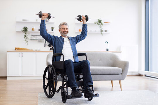 Mature Caucasian man in wheelchair lifting dumbbells during fitness activity at home, showcasing positivity, strength, and resilience. Bright and modern environment with natural lighting