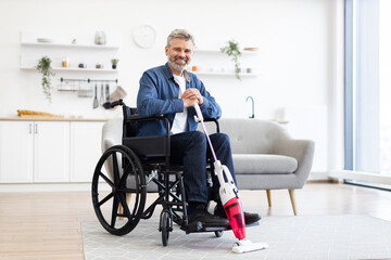 Middle-aged white man in wheelchair vacuuming carpet in modern living room, smiling, teamwork